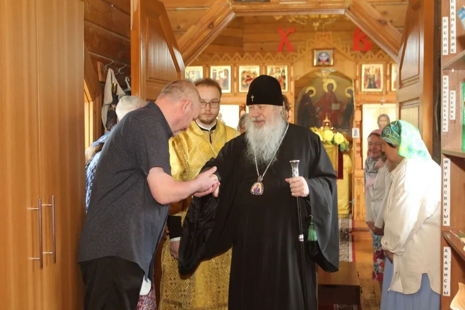 Деревянный притвор храма с вешалкой для одежды и полками, подписанными «Библия», «Евангелие», «Жития святых», «Акафисты»