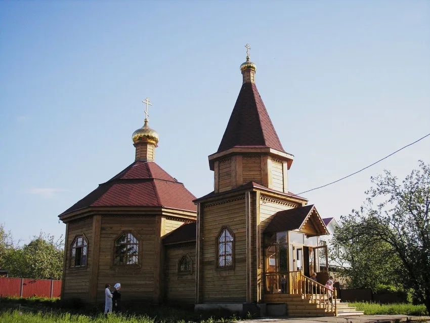 Крытое крыльцо с застеклённой дверью и деревянными ступенями у входа в храм, рядом стоят два человека
