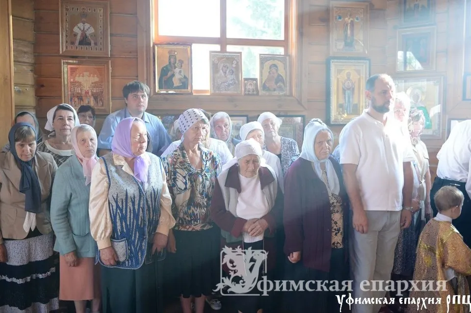 Прихожане стоят в деревянном храме на богослужении, видны иконы на стенах
