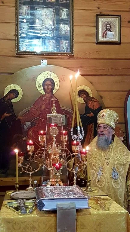 Архиерей в золотом облачении перед иконой праздника и свечами внутри деревянного храма